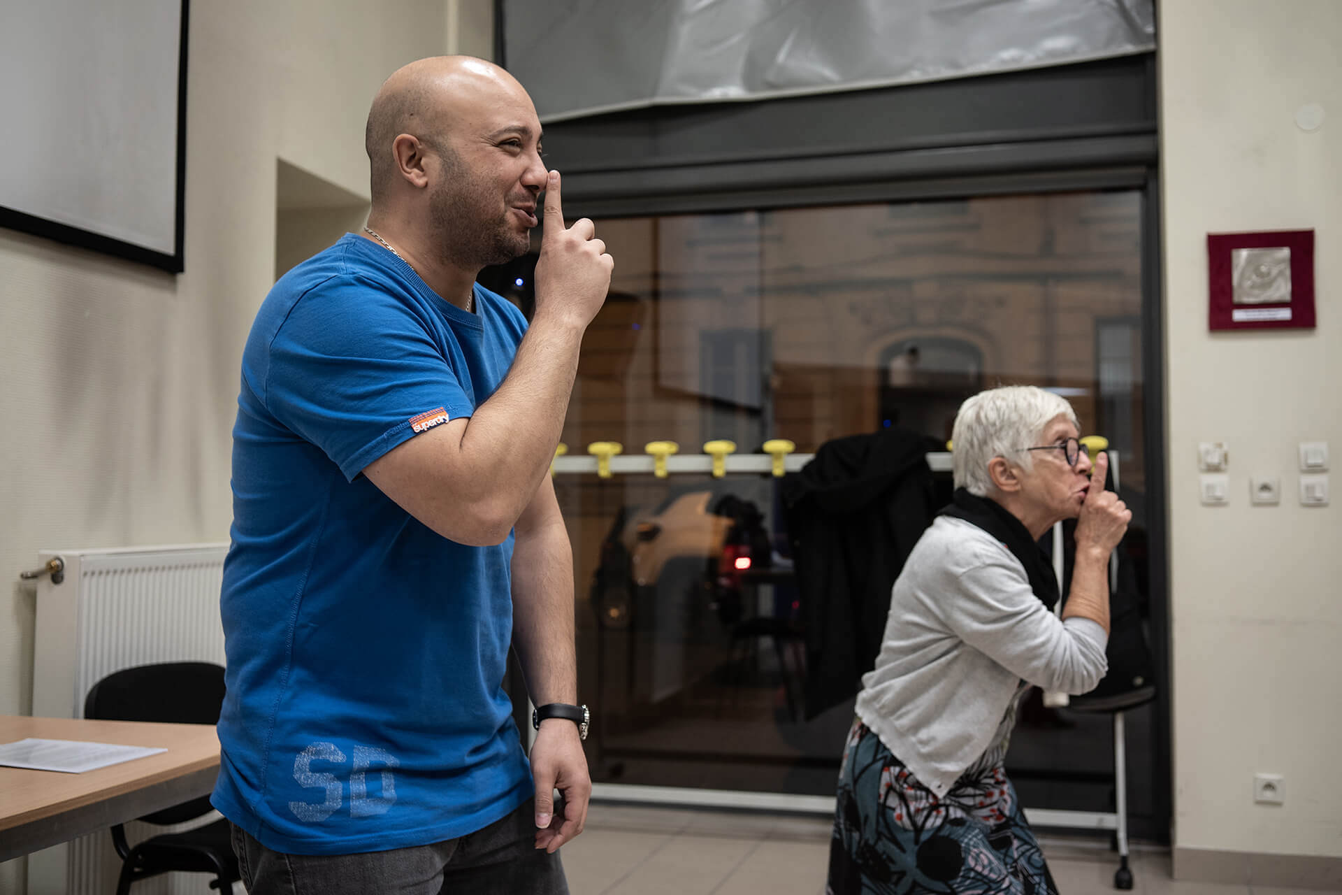 Cours de théâtre dans une des salles de l’association Valentin Haüy, à Lyon. A la demande de Jérôme (le professeur), Nabil, malvoyant, à gauche sur la photo, et Martine font le signe, doigt sur la bouche, que l’on réalise parfois pour demander le silence. Nabil sourit de l’exercice tandis que Martine affiche un peu plus de sérieux.