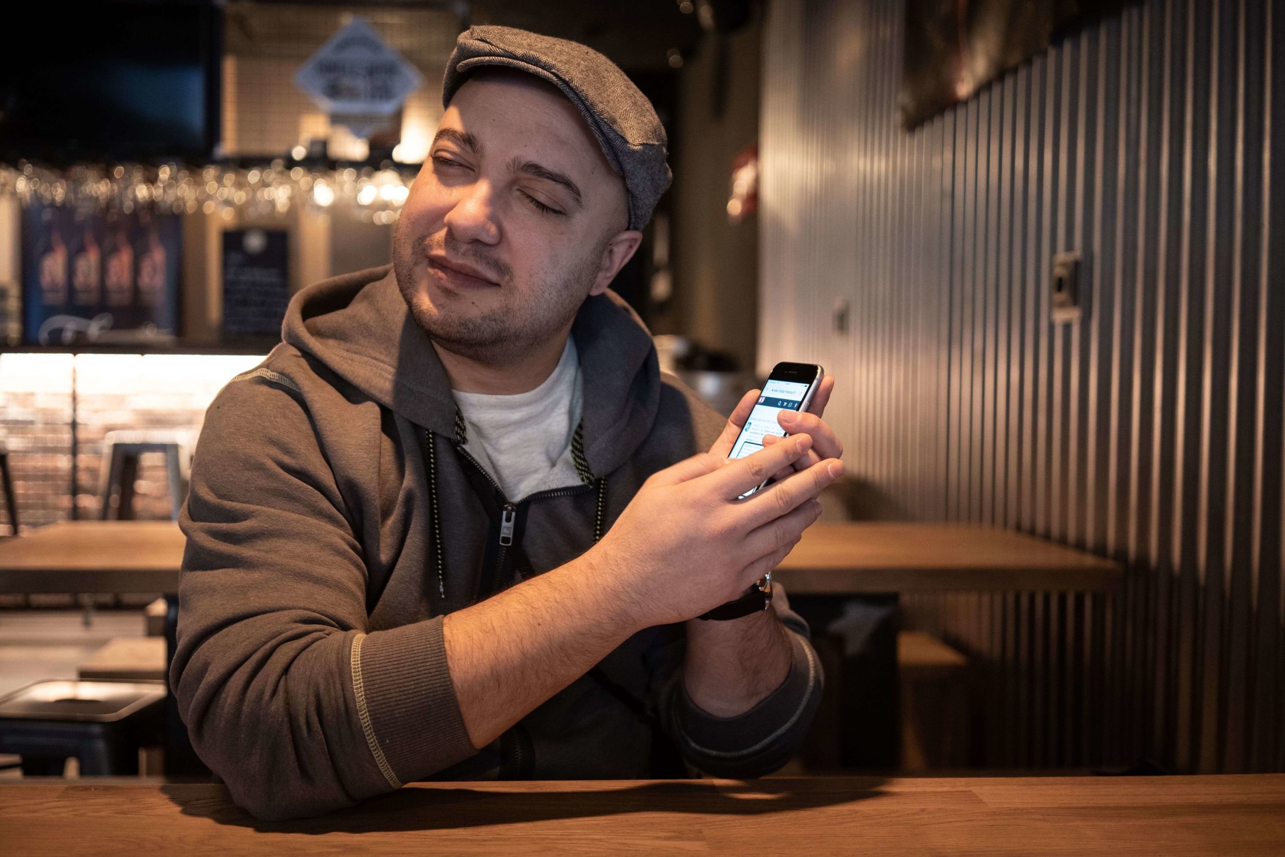Nabil, 34 ans, est assis à la table d'un bar de Lyon. Il porte une casquette et tient un téléphone entre ses mains.